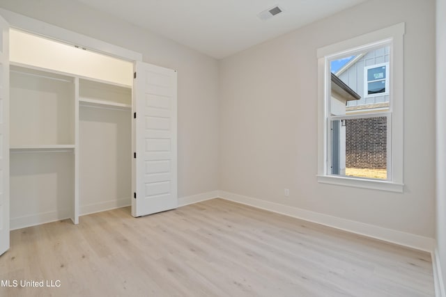 unfurnished bedroom featuring light hardwood / wood-style flooring, multiple windows, and a closet