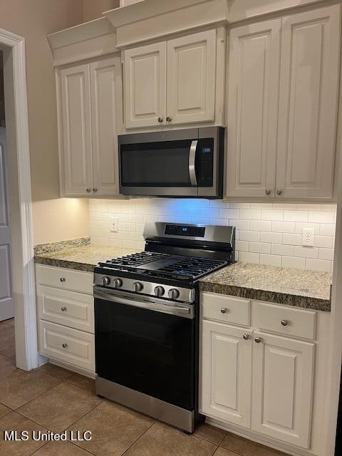 kitchen with light tile patterned floors, backsplash, white cabinetry, and stainless steel appliances