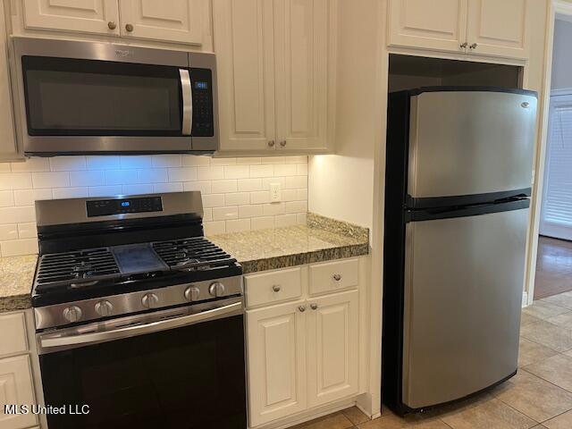 kitchen featuring light tile patterned flooring, decorative backsplash, appliances with stainless steel finishes, and white cabinetry