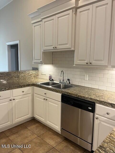 kitchen with tile patterned floors, a sink, stainless steel dishwasher, white cabinetry, and decorative backsplash