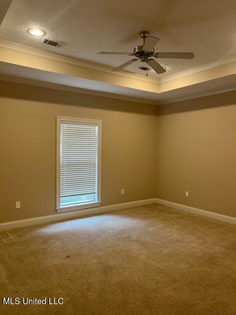 carpeted spare room featuring visible vents, a ceiling fan, a tray ceiling, crown molding, and baseboards