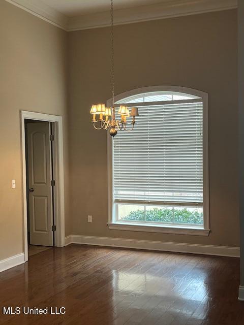 empty room with a chandelier, crown molding, baseboards, and wood finished floors