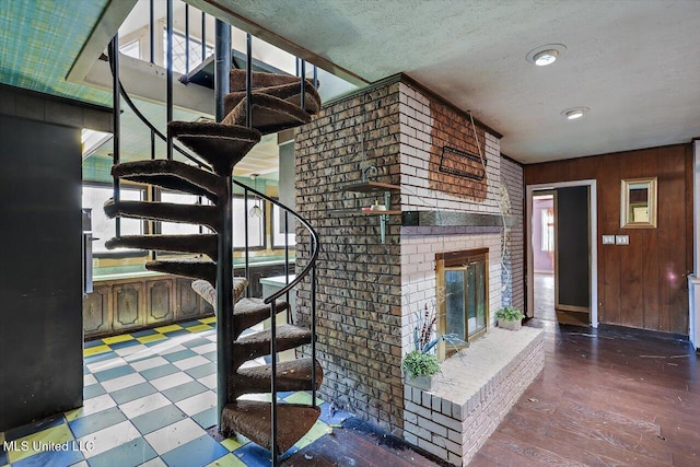 stairway featuring a brick fireplace, a wealth of natural light, a textured ceiling, and wooden walls