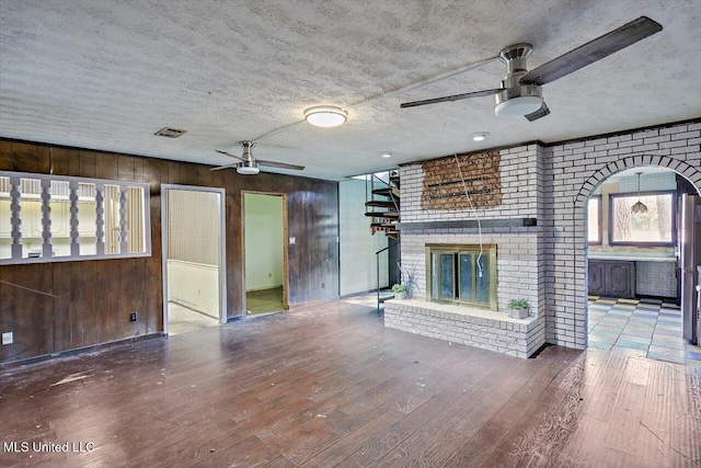 unfurnished living room featuring hardwood / wood-style floors, a textured ceiling, a fireplace, and wood walls