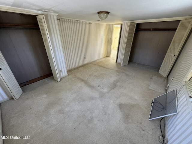 unfurnished bedroom featuring multiple closets and light colored carpet