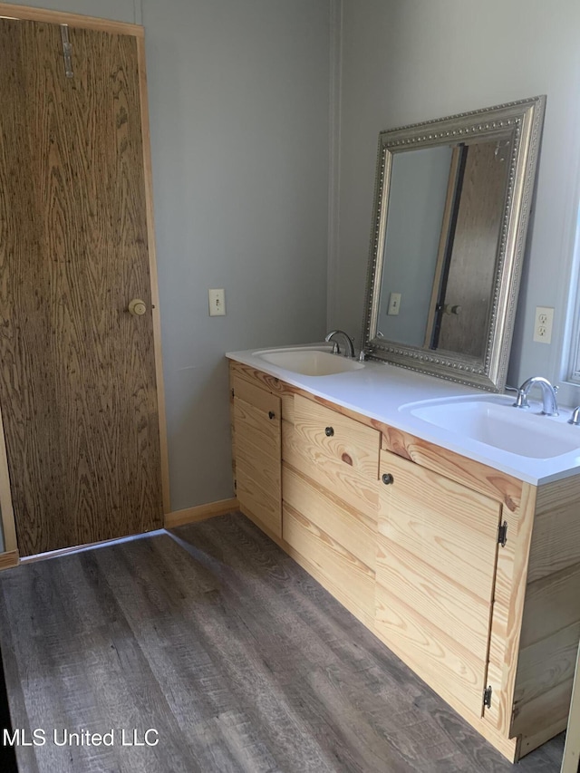 full bathroom featuring double vanity, wood finished floors, baseboards, and a sink