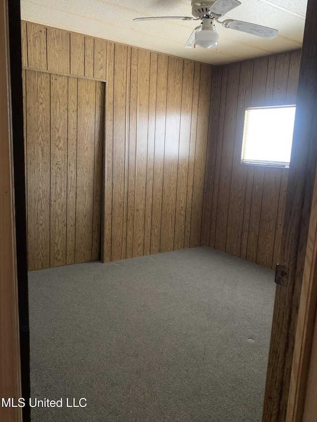 unfurnished room with wooden walls, carpet, and ceiling fan