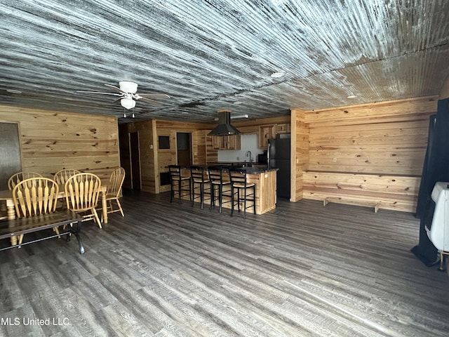 dining area with dark wood finished floors, wooden walls, heating unit, and ceiling fan