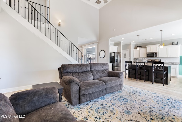 living room with crown molding, light wood finished floors, baseboards, a towering ceiling, and stairs