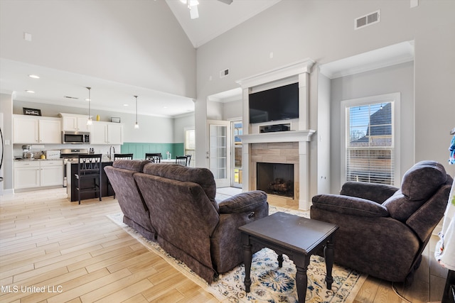 living room featuring visible vents, high vaulted ceiling, a fireplace, light wood-style floors, and crown molding