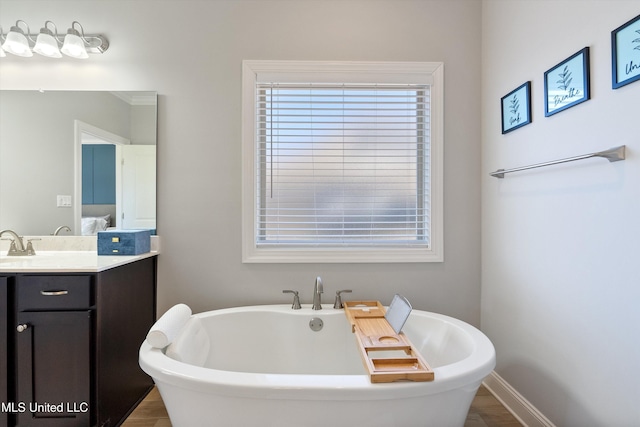 ensuite bathroom with vanity, wood finished floors, baseboards, ensuite bath, and a freestanding bath