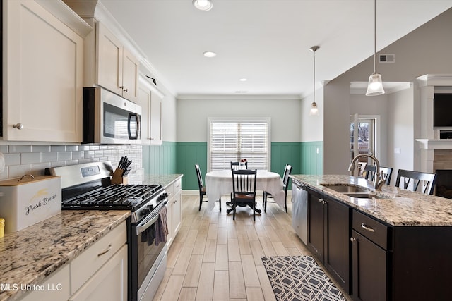 kitchen featuring light wood finished floors, visible vents, wainscoting, stainless steel appliances, and a sink