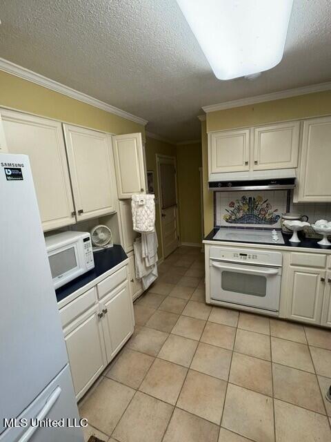 kitchen with under cabinet range hood, light tile patterned floors, ornamental molding, white appliances, and white cabinets