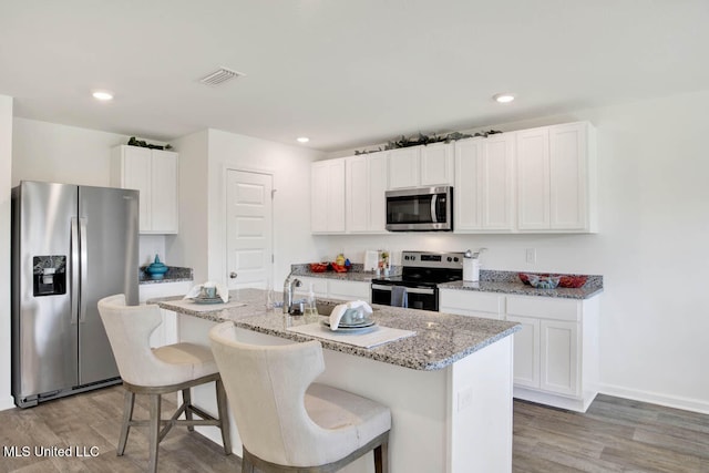 kitchen featuring white cabinetry, a kitchen island with sink, wood-type flooring, a kitchen bar, and stainless steel appliances