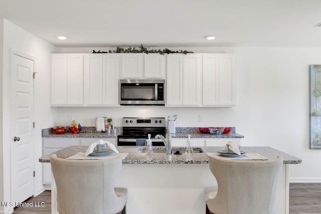 kitchen with white cabinetry, appliances with stainless steel finishes, dark hardwood / wood-style flooring, and an island with sink