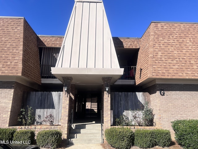 entrance to property with a shingled roof, mansard roof, and brick siding