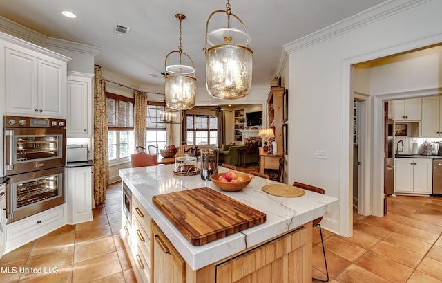 kitchen with hanging light fixtures, light tile patterned flooring, ornamental molding, and a center island