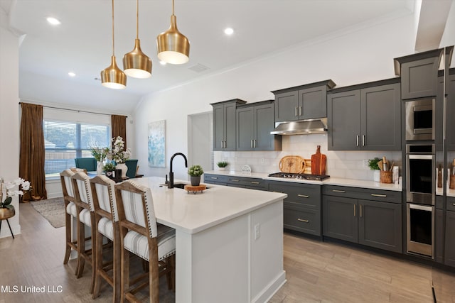 kitchen featuring a center island with sink, sink, pendant lighting, a kitchen bar, and light wood-type flooring