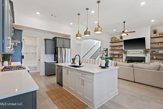 kitchen with light hardwood / wood-style floors, a center island with sink, sink, appliances with stainless steel finishes, and decorative light fixtures