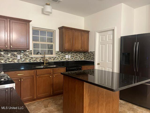 kitchen featuring backsplash, black refrigerator with ice dispenser, sink, and a kitchen island