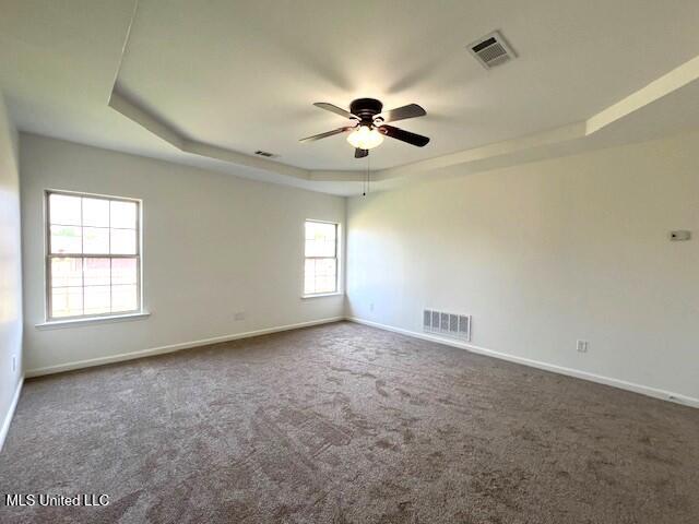 empty room with ceiling fan, a raised ceiling, and carpet floors