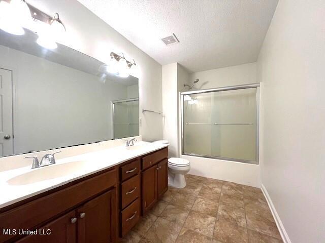 full bathroom featuring vanity, a textured ceiling, enclosed tub / shower combo, and toilet