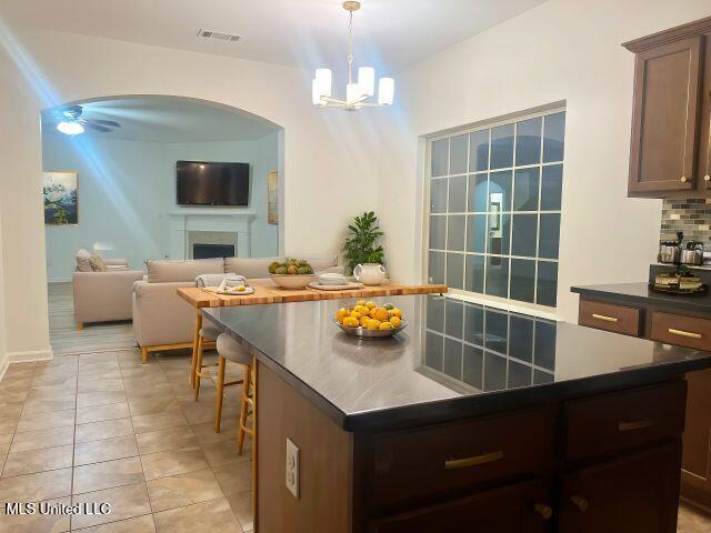 kitchen featuring pendant lighting, dark brown cabinets, a center island, decorative backsplash, and ceiling fan with notable chandelier