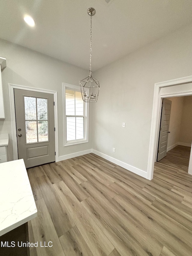 unfurnished dining area with an inviting chandelier and light wood-type flooring