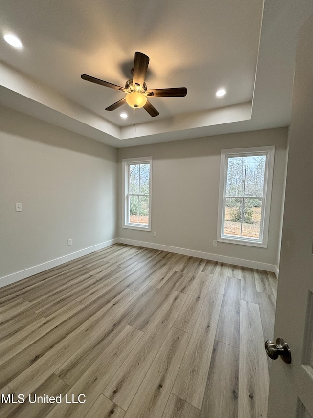 empty room with ceiling fan, a raised ceiling, and light hardwood / wood-style flooring