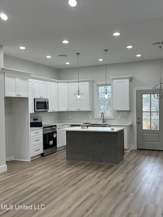 kitchen with stainless steel appliances, a center island, hanging light fixtures, and white cabinets