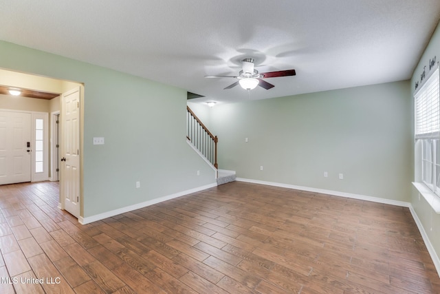 spare room featuring baseboards, wood finished floors, stairs, and ceiling fan