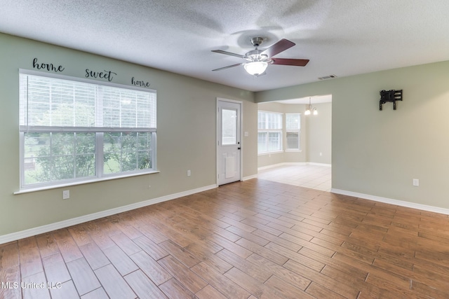 empty room featuring a textured ceiling, wood finished floors, ceiling fan with notable chandelier, baseboards, and visible vents