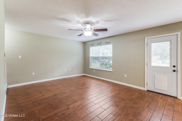 empty room featuring dark wood-type flooring, a textured ceiling, a ceiling fan, and baseboards