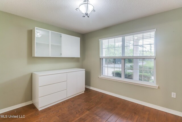 unfurnished bedroom featuring baseboards, a textured ceiling, and dark wood-style flooring