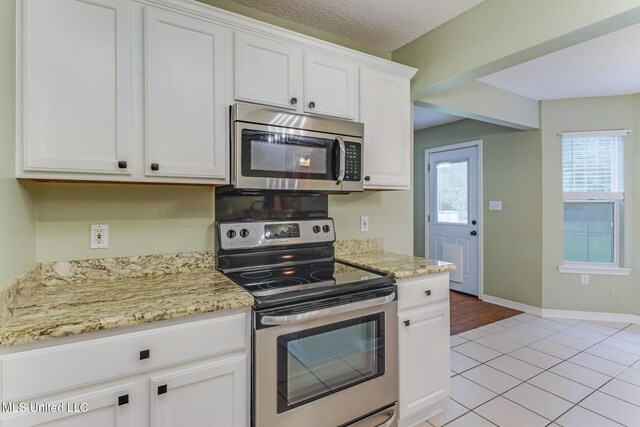 kitchen featuring stainless steel appliances, light stone counters, white cabinetry, and light tile patterned floors