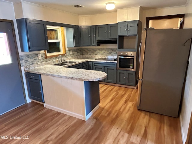 kitchen with stainless steel appliances, tasteful backsplash, sink, and light wood-type flooring