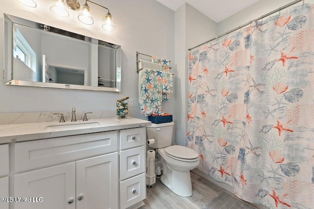 bathroom with a shower with shower curtain, hardwood / wood-style floors, vanity, and toilet