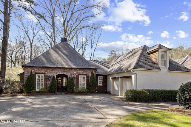 view of front of property featuring driveway, roof with shingles, an attached garage, brick siding, and a chimney