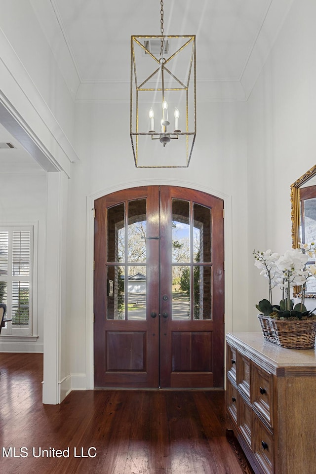 foyer featuring dark wood finished floors, a notable chandelier, french doors, and ornamental molding