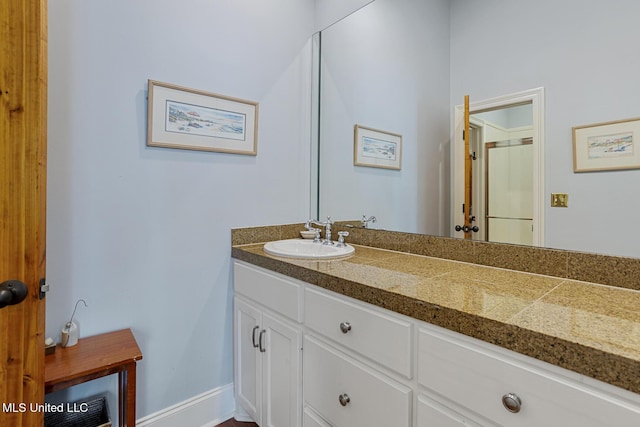 bathroom with vanity, baseboards, and a shower with door