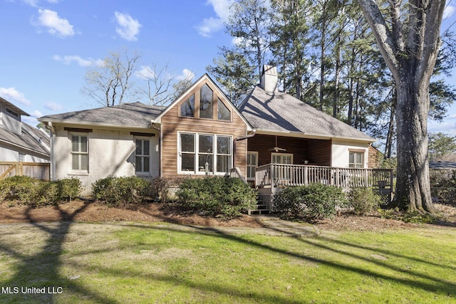 view of front of property with a shingled roof, a front yard, a wooden deck, and a chimney