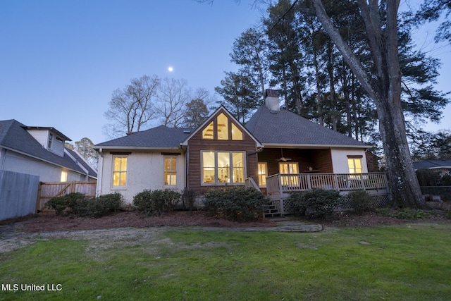 back of property featuring fence, a wooden deck, a shingled roof, a chimney, and a lawn