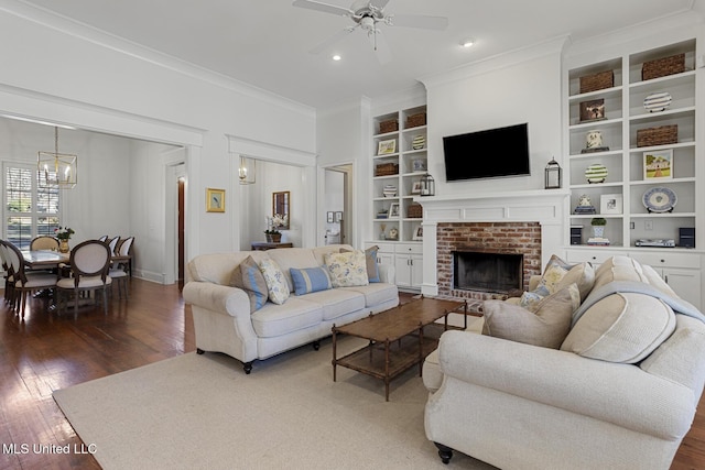 living area with built in shelves, a fireplace, hardwood / wood-style flooring, crown molding, and ceiling fan with notable chandelier