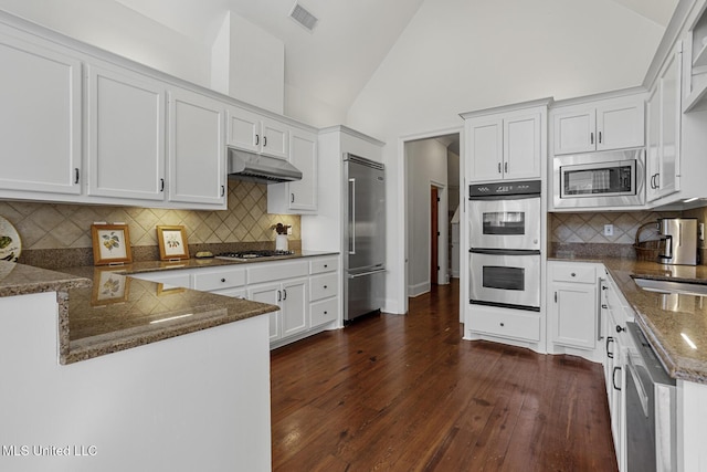 kitchen featuring visible vents, under cabinet range hood, dark stone countertops, white cabinetry, and built in appliances