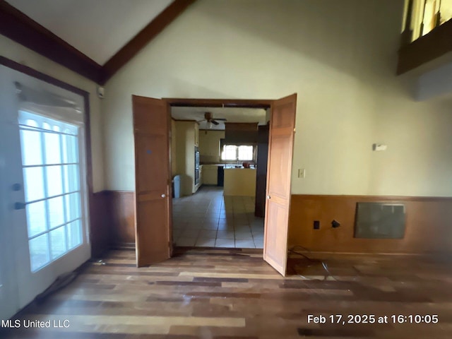 interior space with a ceiling fan, high vaulted ceiling, wood finished floors, and wainscoting