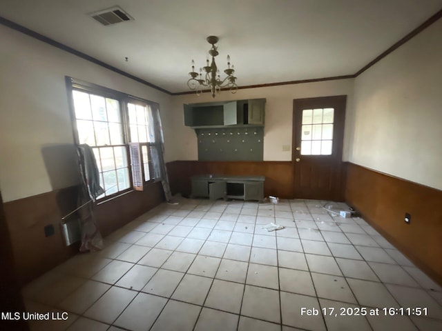 unfurnished dining area with wooden walls, visible vents, ornamental molding, wainscoting, and a notable chandelier