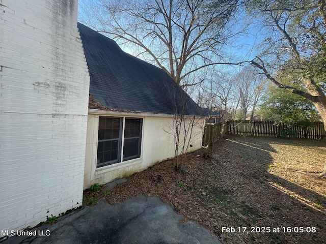 view of side of home featuring fence, brick siding, and roof with shingles