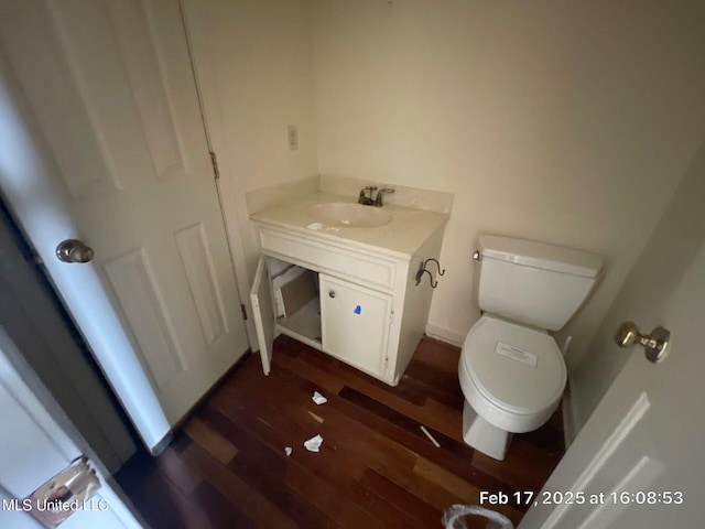 half bath with toilet, wood finished floors, and vanity