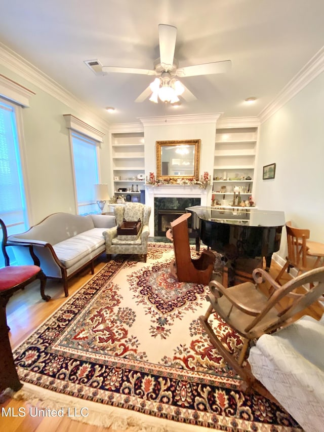 living room featuring built in shelves, ceiling fan, a premium fireplace, and crown molding