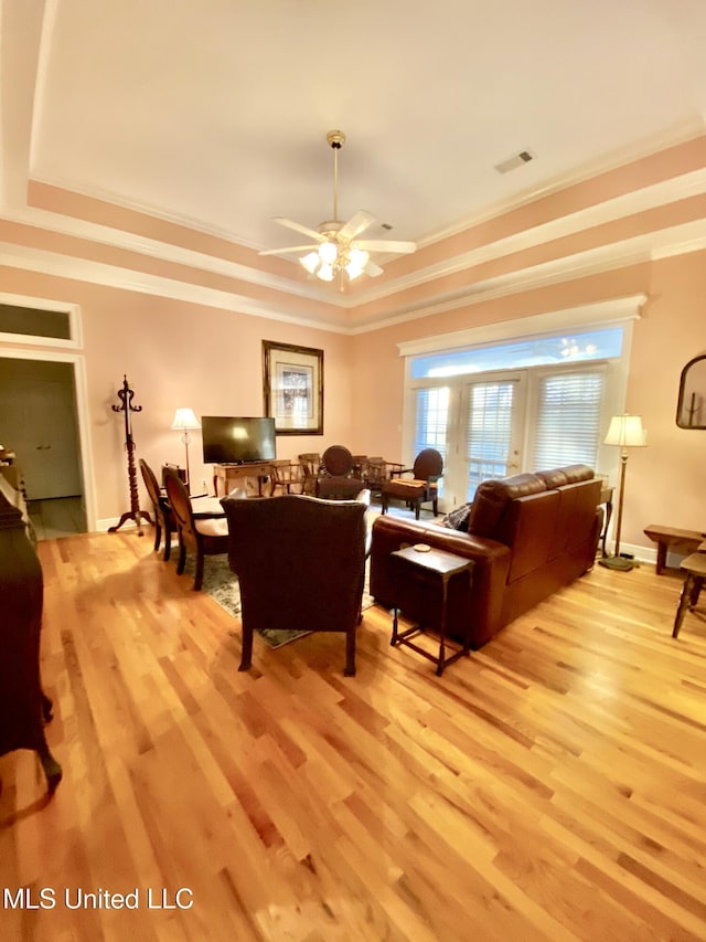 living room featuring crown molding, a tray ceiling, and light hardwood / wood-style flooring